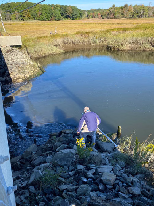 A volunteer navigates rocks to take a water sample off Black Point Road